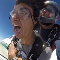 Tandem skydiving student holding on tight and yelling