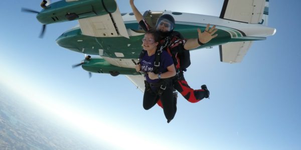 Tandem skydiving instructor spreading his arms as they jump from the plane