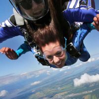 Tandem skydiving student smiles as the wind rushes past her