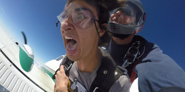 Tandem skydiving student holding on tight and yelling