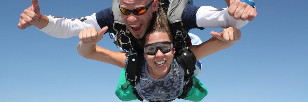 A girl giving two thumbs up while in free fall on a tandem skydive